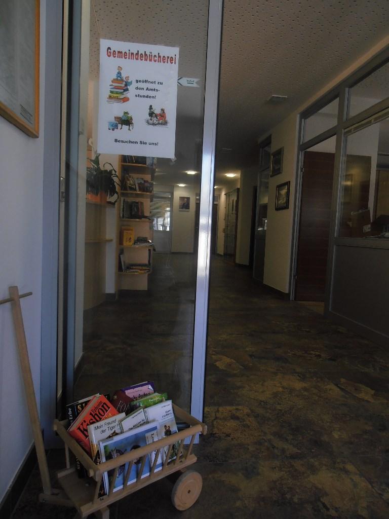 Eingangsbereich Bücherei mit Glastüre halb geschlossen - davor steht ein Kinderleiterwagerl mit Büchern